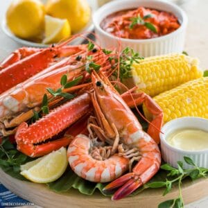 Alt text: "A bright, warm image of a seafood boil featuring shrimp, crab legs, and corn on the cob, garnished with fresh herbs and lemon wedges. The dish is served on a wooden board with a side of melted butter. A bowl of Seafood Boil Sauce is visible in the background, adding to the inviting atmosphere. The footer reads 'dinedecisions.com.'"